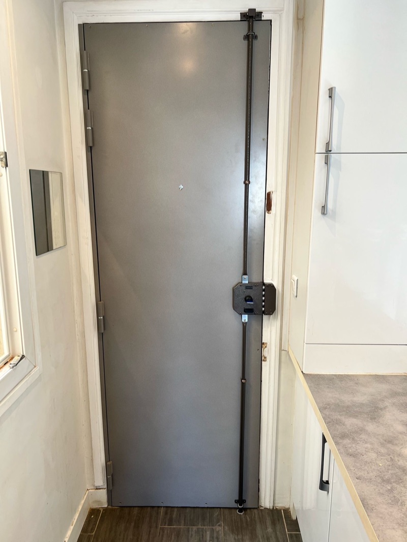Vue intérieure d'une porte blindée grise : serrure multipoints apparente et tringles verticales de crémone courant du haut au bas du vantail — Paris 15e