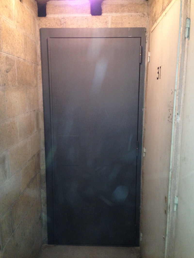 Porte de cave métallique anthracite posée dans un couloir de caves en parpaings, huisserie acier scellée dans la maçonnerie — Charenton-le-Pont