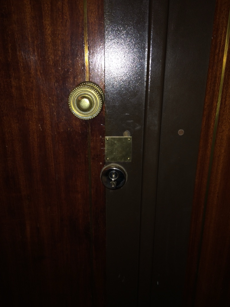 Cylindre chromé et plaque de propreté en laiton sur la cornière brune d'une porte en acajou, bouton de tirage ancien à gauche — Paris 15e