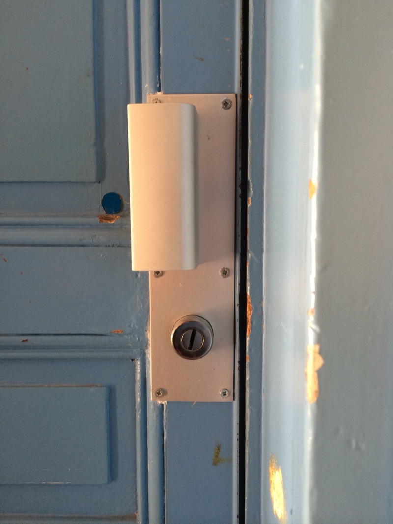 Serrure en applique crème avec bouton de tirage et cylindre, posée sur une porte en bois mouluré peinte en bleu — Paris 15e