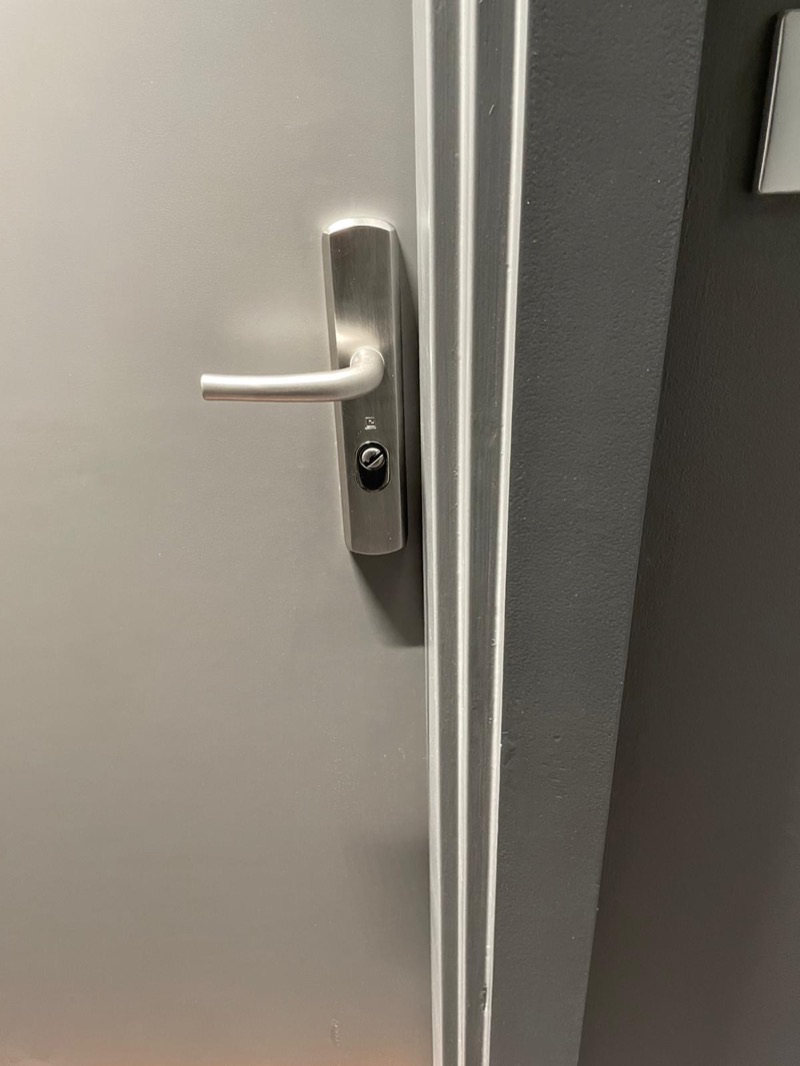 Plaque de poignée blindée en aluminium brossé, béquille et cylindre protégé, posée sur une porte grise — modèle Héraclès Salomé, Boulogne-Billancourt