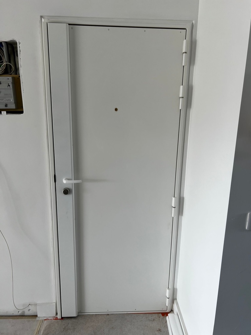 Porte blindée blanche avec carénage vertical sur le chant, béquille et cylindre, dans une entrée en cours de travaux — Charenton-le-Pont