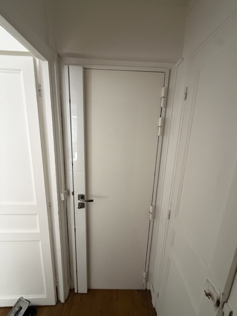 Porte blanche équipée d'une serrure carénée, béquille chromée et cylindre, dans le couloir d'un appartement ancien — Charenton-le-Pont