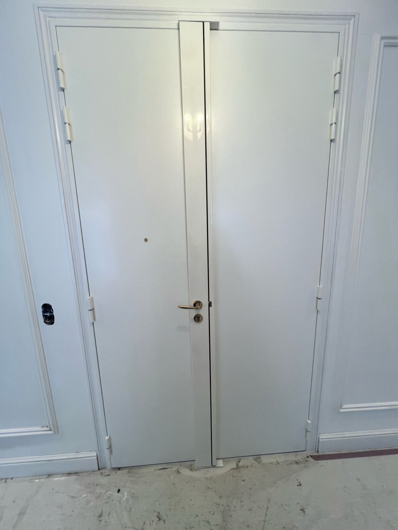 Porte d'entrée blanche à double vantail après blindage, carénage vertical central et béquille laiton, chantier encore en cours — Paris 15e